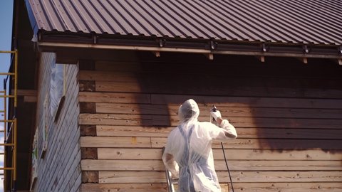 a worker paints a house with paint from an airless pump