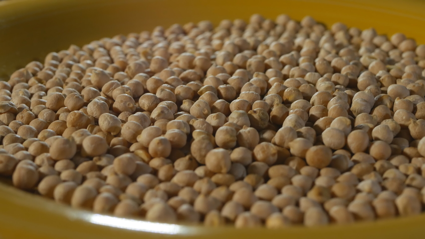 A large yellow plate filled with chickpeas rotates slowly. The chickpea grain is evenly lit and harmonizes well with the color of the plate. Vegetarian food. Eco products