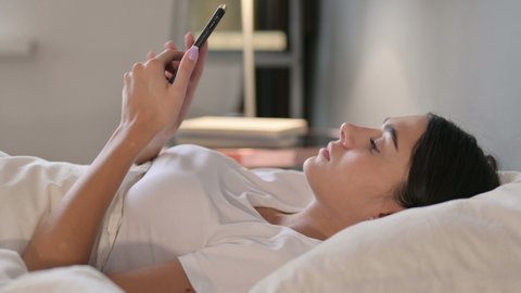 Smartphone use by Latin Woman Laying in Bed 