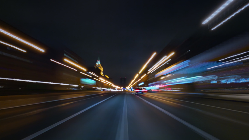 Amazing motion timelapse of a speedy night drive in a big city, front view from the car to the road. Glittering streets and building lights turning into beautiful light trails.  Royalty-Free Stock Footage #1062027631