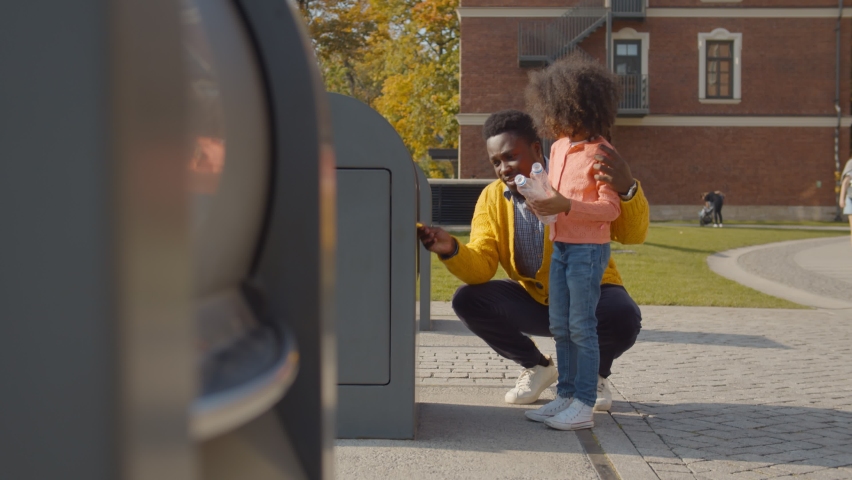 African father teaching cute preschool daughter throwing plastic bottle in recycling trash bin. Side view of afro-american dad and little girl throwing garbage in container outdoors | Shutterstock HD Video #1062029611