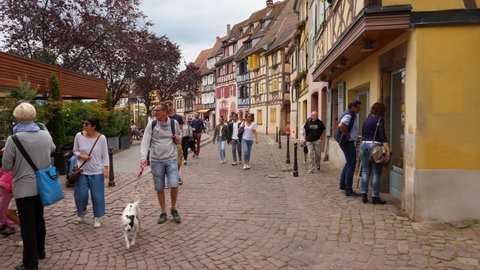 COLMAR, FRANCE - AUGUST 17, 2019: Unidentified tourists stroll around Krutenau area at Colmar town, first person view camera. Beautiful old half-timbered buildings, facades painted in different colour