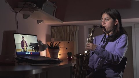 Young Woman is learning a musical instrument online. Video call with saxophone teacher. Remote learning from home  Online education in times of Coronavirus