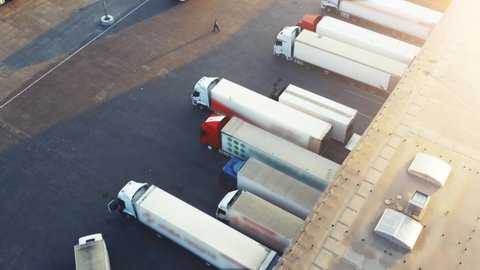 Aerial view of semi-trailers trucks stands at warehouse`s ramps for load/unload goods in large logistics park with loading hub