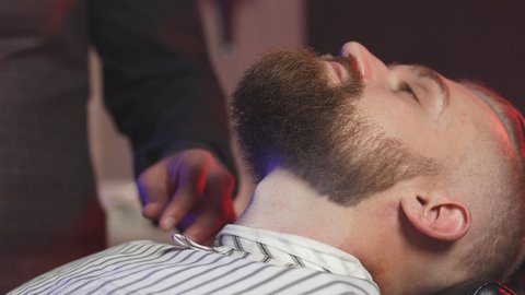 Handsome man on chair of barber having procedure of shaving, get beauty procedures in barber shop
