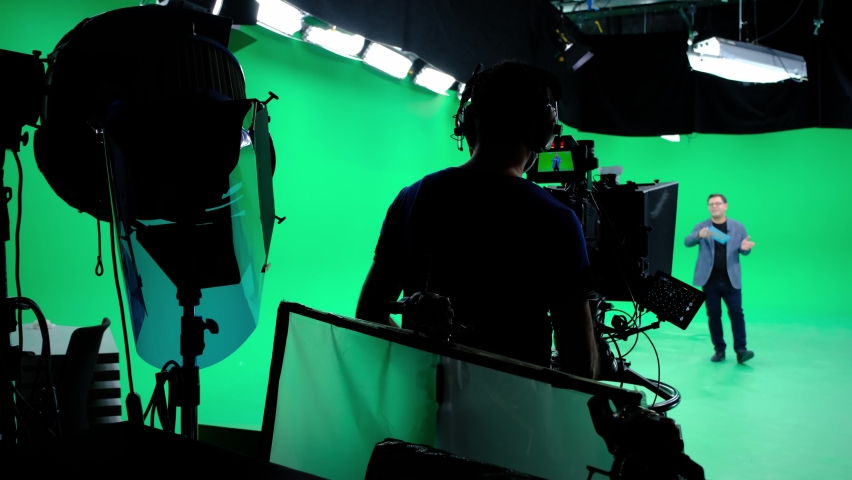 The cameraman follows the announcer in a professional green screen studio. The professional looks all the shooting equipment; lights, camera, green screen, monitors, filters Royalty-Free Stock Footage #1062035326