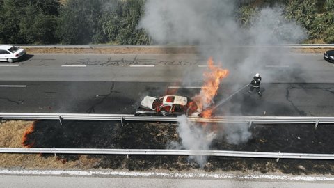 Firefighters extinguish burning car on highway following serious car accident on hot summer day aerial view. Fire truck came to the rescue. Flow of cars on track. Problem is on road. Traffic incident