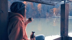 The girl is resting on a hike. Drinks tea from a thermos on the shore of a mountain lake. Slow motion video.