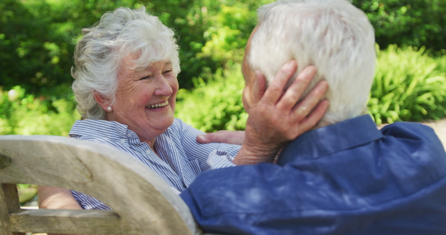Happy senior caucasian couple in garden, smiling, embracing, sitting on bench on sunny day in slow motion. enjoying time in garden during coronavirus covid 19 lockdown. | Shutterstock HD Video #1062040747