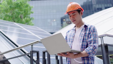 Engineer or construction worker Asian man is using  laptop to check solar cell replacement power system. Solar cell technology for building Or industrial factory. Hard hat help protect with operation