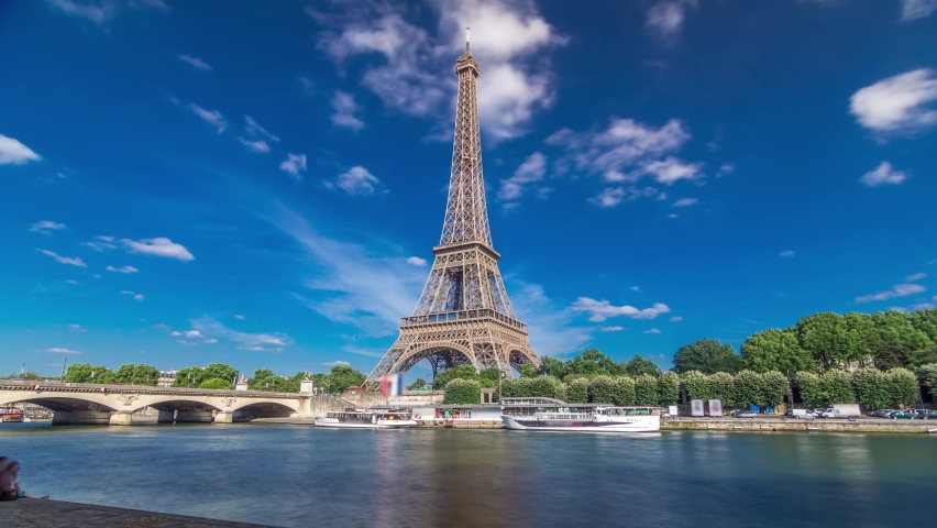 The Eiffel tower timelapse hyperlapse from waterfront at the river Seine in Paris. Ship and boats on river at sunny summer day
