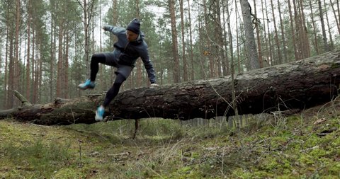 man running on forest trail and jump over old fallen tree. slow motion slider shot