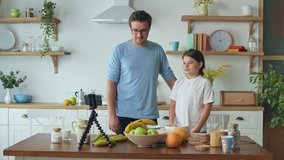 A Father with a Cute Daughter is Blogging About Cooking. Video Blog About Healthy Eating. A Father with a Child is Watching an Online Video Blog. A Father Teaches His Daughter to Cook.