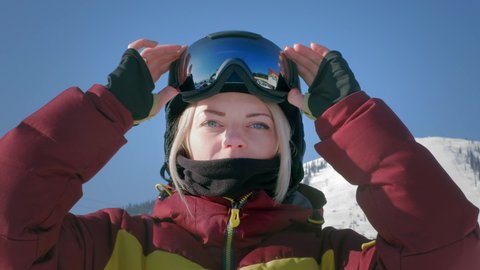 A beautiful girl puts on winter goggles or a mask for snowboarding. The concept of victory in sports, winning, win. Getting ready for skiing on a snowy slope. Winter travel at the ski resort.