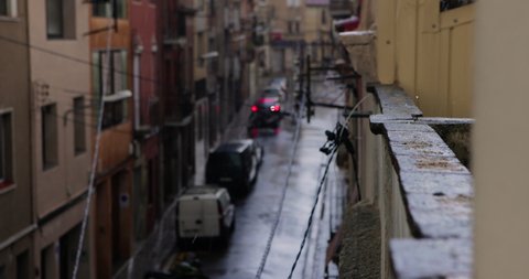 Slow motion of a hail rain hitting a roof edge of a spanish town building during a storm. Top view of a street of with cars parked..