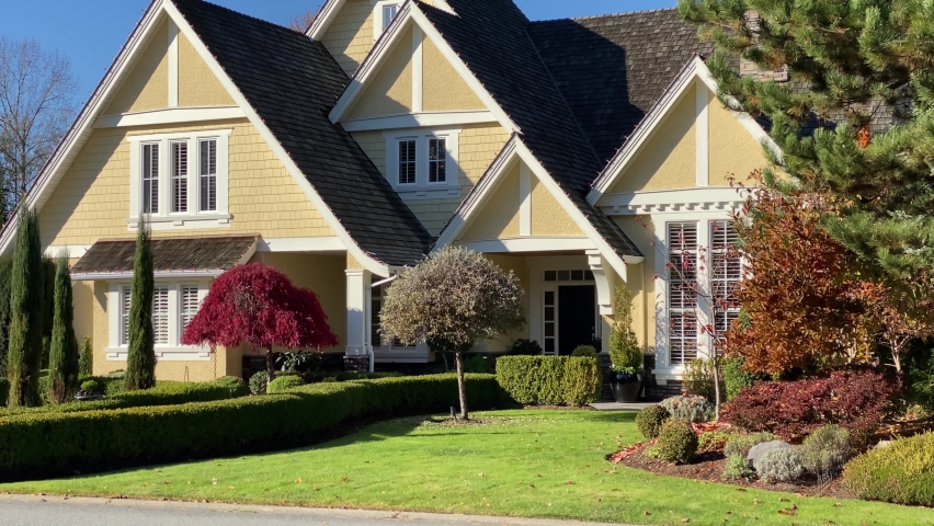 Establishing shot. Fragment of two story yellow luxury house with curved path, red tree and nice landscape in Vancouver, Canada. Day time on September 2020. Shot 2 of 3. Still camera view. H.264.