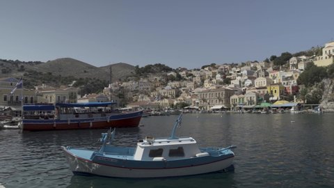 Chalki / Halki island, Greece - September 25, 2020: Pan shot of bright color houses with ceramic-tiled roofs and wooden windows constructed on rusty hills in Dodecanese Island. flat ungraded
