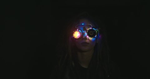 Woman in steampunk VR glasses in darkness. Female with messy hair wearing glowing VR goggles walking along dark corridor of abandoned building and exploring cyberspace