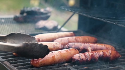 Grilled sausages roasting on barbecue grill outdoors. BBQ. Grilled food fried and smoked in charcoal grills. Turns grill over with tasty delicious sausages. concept street food for picnic and camping ஸ்டாக் வீடியோ