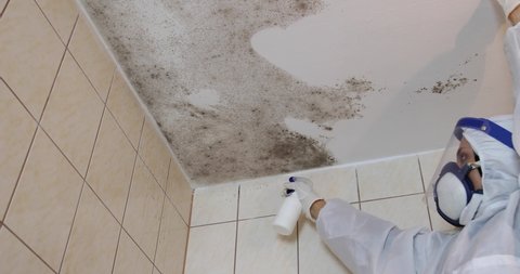 Footage of molded bathroom and a person in professional protection suit spraying chemicals to kill the mold and fungus.