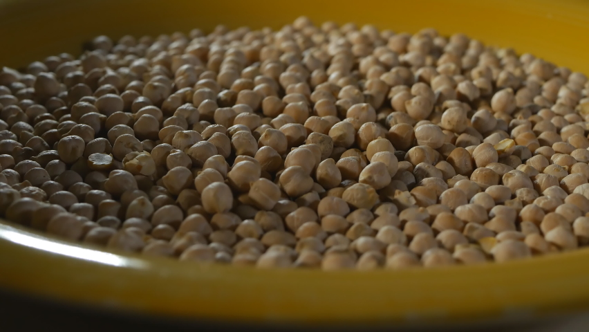 a lot of chickpeas are poured into a large yellow plate. The plate of chickpeas slowly rotates around. View from the bottom point. The lighting is light with soft shadows. 4k