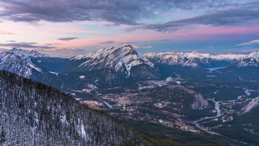 Town of Banff dusk to light up at night, scenery view in snowy winter season. Cascade Mountain and surrounding mountains in background. Banff National Park, Alberta, Canada. 4K Time-lapse zoom in. Royalty-Free Stock Footage #1062054706