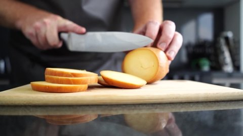 Caucasian male hands slice provolone cheese in a beautiful kitchen ambient