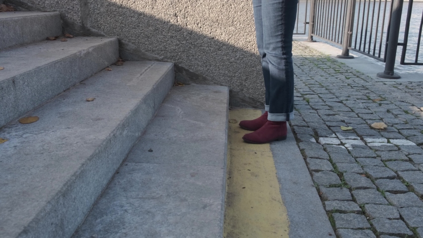 Female legs in burgundy boots and blue jeans climb the stone stairs on a sunny autumn day. No people | Shutterstock HD Video #1062056524