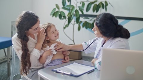 Female Doctor Pediatrician Using Stethoscope Listen to the Heart of Happy Healthy Cute Kid Girl at Medical Visit With Mother in the Hospital. Mother With Kid at Visiting Pediatrician.