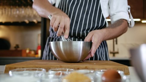 Close-up Man Hand Chef Mixing Food Ingredient In Steel Bowl. Baker Hands Knead Dough with a Whisk in Kitchen. Home Cooking Concept. Adult Cook Mix Knead for Preparing Baking Meal on Slow Motion 4k