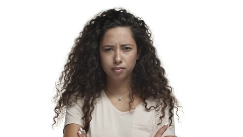 Close-up of young skeptical woman with long curly hairstyle, cross arms on chest defensive and frowning, rolling eyes from something annoying, standing over white background