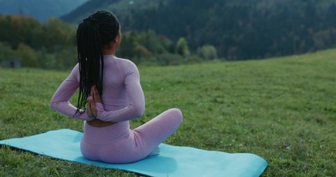Afro-american fitness sportswoman sitting on grass hands back meditating practice enjoying nature connection, fresh air and calm mind. Outdoor yoga. Sport activities. Healthcare.