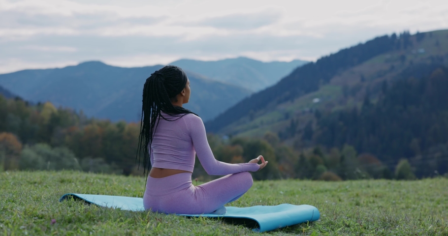African american calm peaceful sportswoman sitting on mountain peak enjoying fresh air meditating for zen, healthcare and welbeing. Motivation. Active lifestyle. Royalty-Free Stock Footage #1062063904