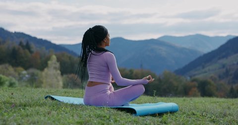 African american calm peaceful sportswoman sitting on mountain peak enjoying fresh air meditating for zen, healthcare and welbeing. Motivation. Active lifestyle.