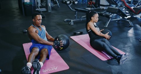 Young determined afro-american athletic couple performing russian twist exercise with fitness balls at gym club. Sports team. Cooperation. Active sports concept.