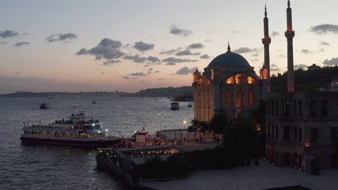 Beautifully lit Ortakoy Mosque with Yellow light on Bosphorus riverside revealing incredible Sunset over Istanbul, Aerial Establishing Shot, Istanbul, Turkey on September 17th 2020