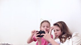 a teenage girl plays an online game on a mobile phone with a fun little sister, modern technology and children's games in quarantine.