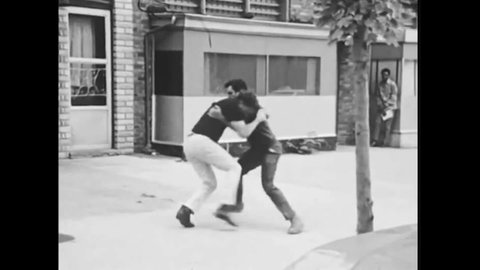 CIRCA 1970s - Police officers increase the tension in a fight between two men outside of a bar, and police officers reduce tension in a fight.