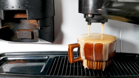 Close up of coffee machine pours coffee into a brown cup. coffee spills over the edge of the cup (overflow)