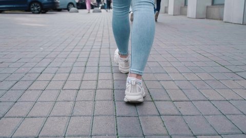 Rear back view feet of woman while walking commuting to work. Confident female in sneakers shoes being walking down the street 4k