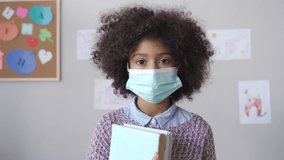 Cute small elementary reopen school pupil african american kid child girl wearing face mask looking at camera standing in classroom. Children safety for covid protection, headshot close up portrait. - Powered by Shutterstock - Get 15% off with code: PIKWIZARD15