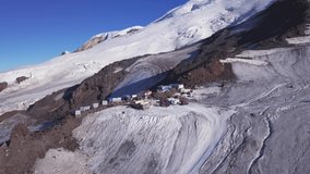 A row of houses built on a snowy mountain slope on blue sky background. Clip. Aerial view of garage buildings and machines located high in the mountains.