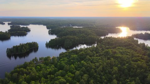 Aerial clip of multiple forested islands on a lake, with the sun glowing in the sky