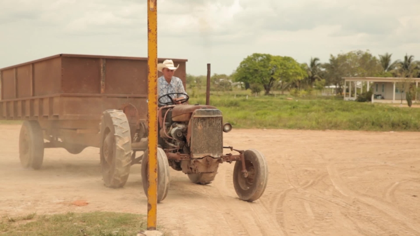 Mennonite daily routine. Young man is driving tractor with a cart. Man is driving on a field. A man transports cargo on an old tractor.