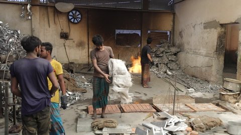 DHAKA, BANGLADESH - OCTOBER 20, 2020: Workers in a sweatshop industrial factory in Bangladesh are melting iron and aluminium in an open fire pit under hot and dangerous and unhealthy circumstances 