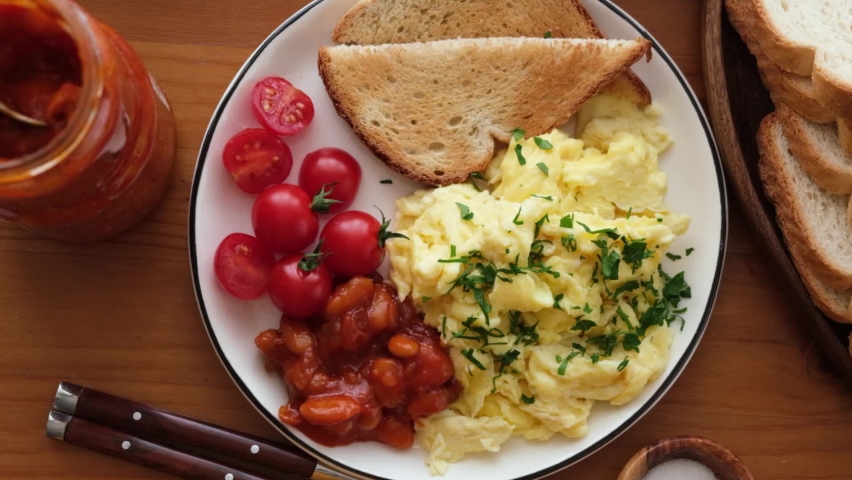 Breakfast scrambled eggs, bread toast, tomatoes and beans on a plate. Top view. Tasty breakfast food Royalty-Free Stock Footage #1062087598