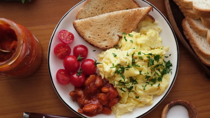 Breakfast scrambled eggs, bread toast, tomatoes and beans on a plate. Top view. Tasty breakfast food | Shutterstock HD Video #1062087598