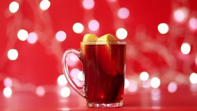 A glass of mulled wine made of red wine stands against a background of red and sparkling garlands