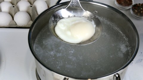 Recipe for cooking poached eggs. Boiled egg take out from boiling water in saucepan. Close-up.