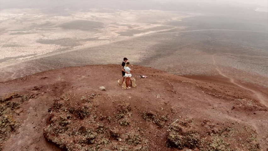 Aerial footage of a couple standing on top of Montana Bermeja, overlooking playa de las conchas on the beautiful Spanish island of La Graciosa
